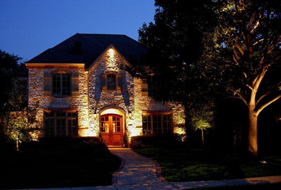 The stone face of a 2-story home illuminated by outdoor lighting