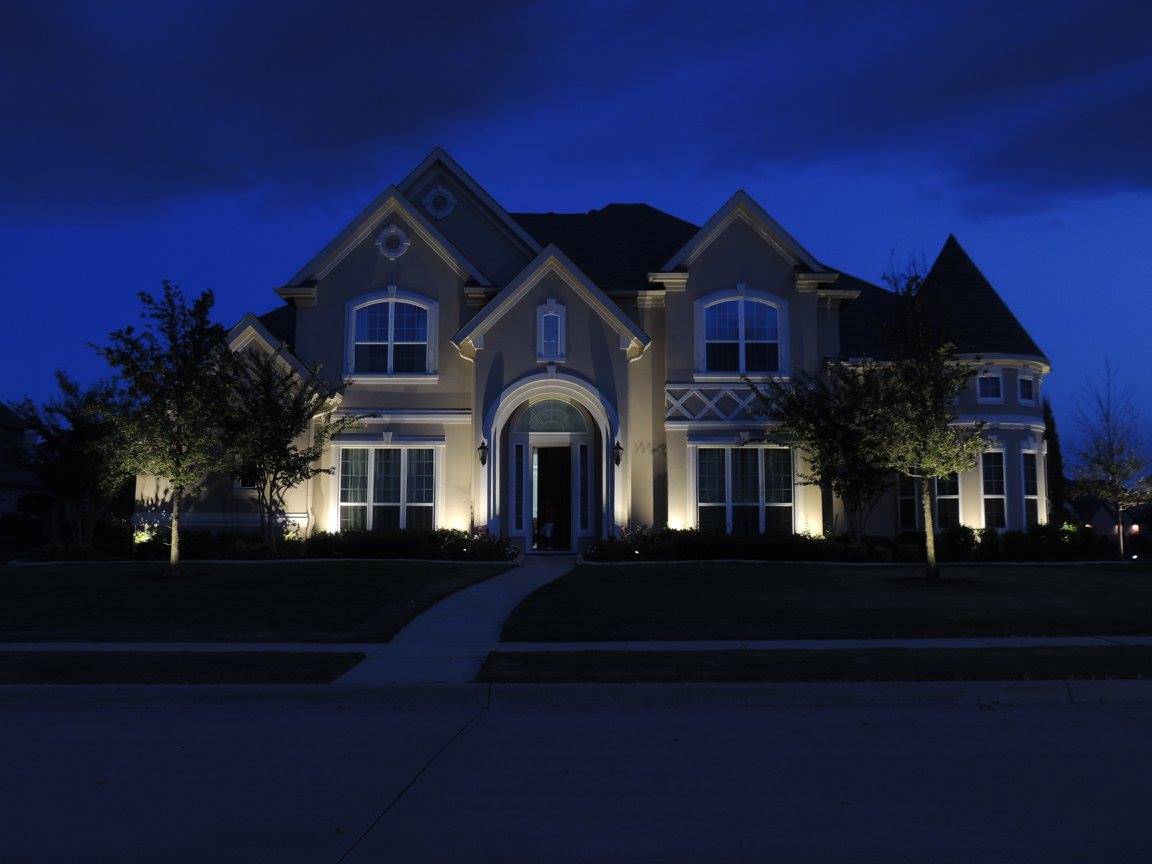 A suburban home at dusk is illuminated by exterior lighting