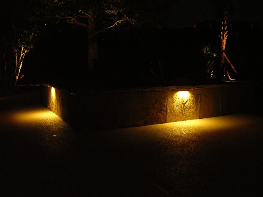 Lighting fixtures on a stone wall light up a pathway