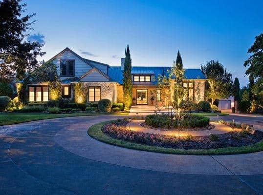 a beautiful well-lit home and circular driveway with landscaping