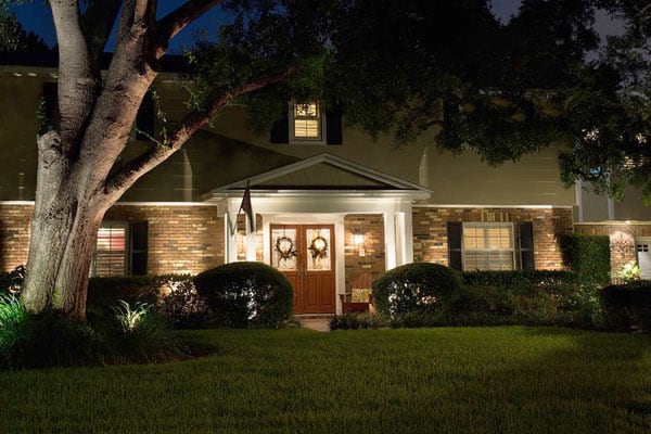 A Well-lit tree stands in front of a colonial home