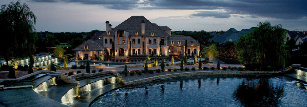 Waterside mansion lit up at night with beautiful landscaping