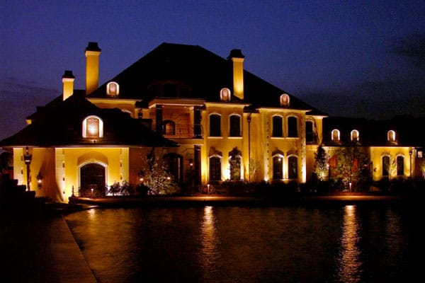 Two-story home with pond in front at night lit up by security lighting