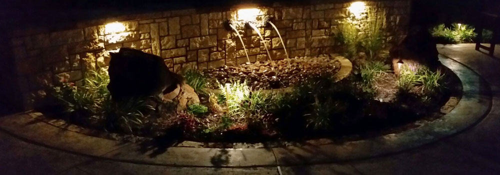 Well-lit water feature with water pouring from stone wall